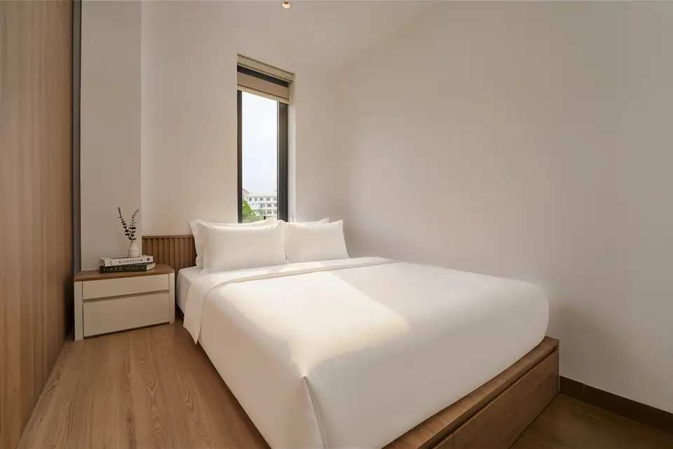 A crisp white double bed on an oak platform, beside a window